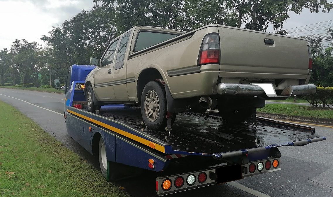 flatbed tow truck towing a beige truck